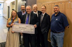 Taylor Woodward holding a novelty check & SHEF Board smiling for the Teacher Excellence Grant presentation at SHMS